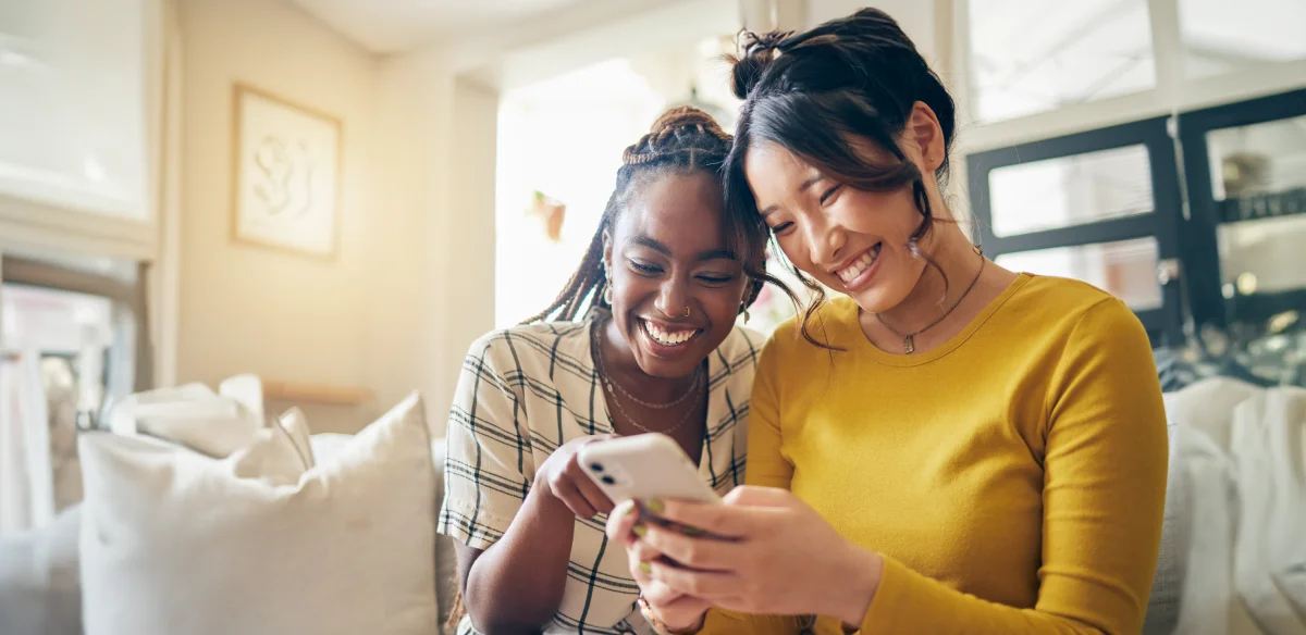 Two girls smiling and looking at their cellphone